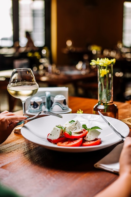 Woman eating tomato salad with mozzarella and mint served with white wine