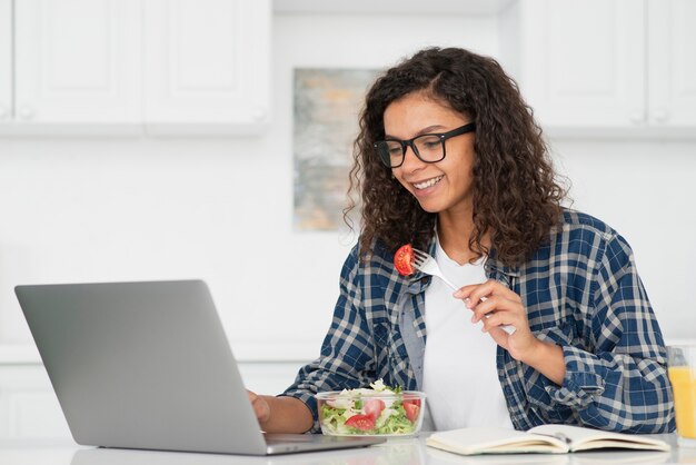 Woman eating vegan salad and working on laptop