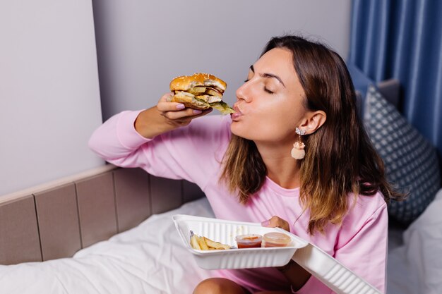 Женщина ест гамбургер дома