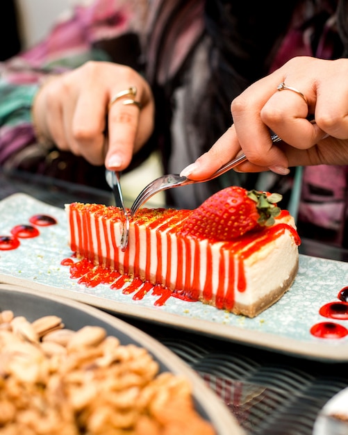 女性はナイフとフォークでイチゴのチーズケーキを食べる