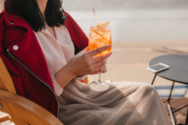 Woman in elegant beige skirt drinking orange beverage in outdoor cafe