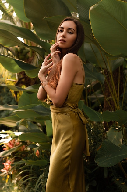 женщина в элегантном шелковом платье позирует в тропическом дождливом тропическом лесу.
