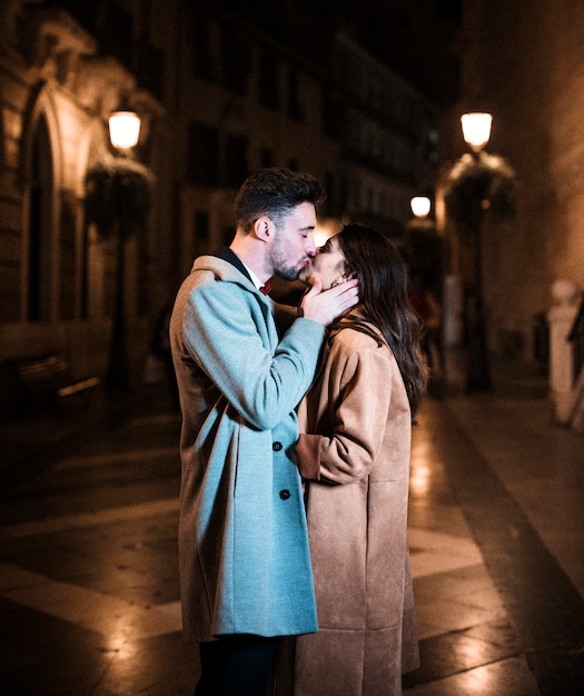 Женщина обнимает и целует с молодым человеком на набережной в вечернее время