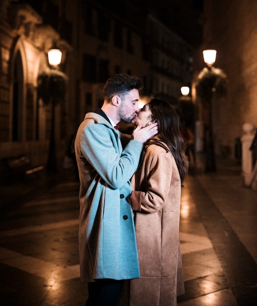 Woman embracing and kissing with young man on promenade in evening