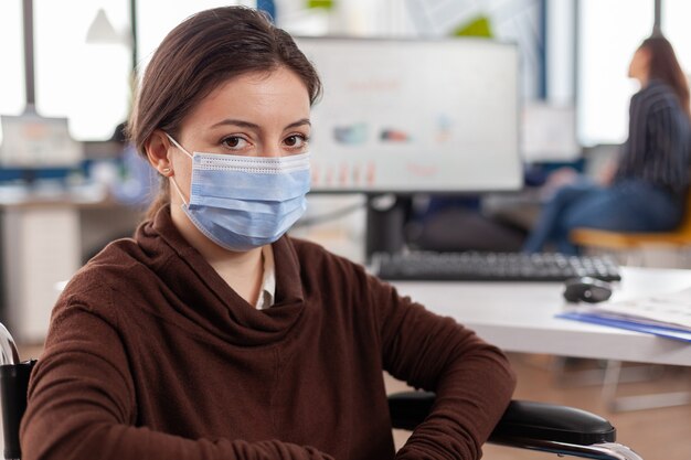 Сотрудник-женщина с ограниченными возможностями с защитной маской от коронавируса смотрит вперед
