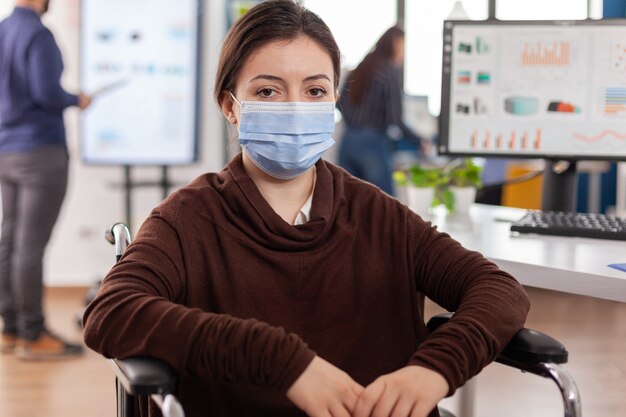 Woman employee with disabilities with protection mask against coronavirus looking at front