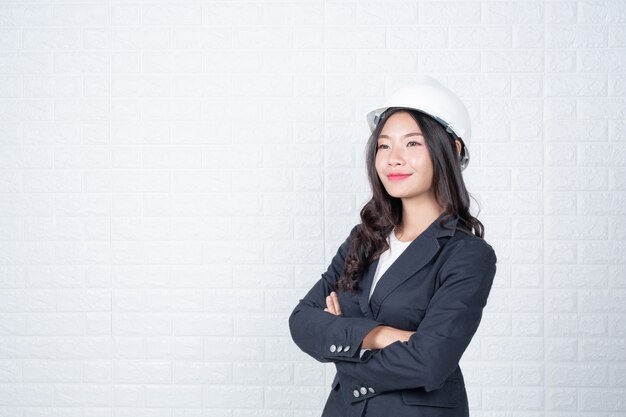 Инженерная женщина, держащая шляпу, отделяет белую кирпичную стену от жестов с помощью языка жестов.