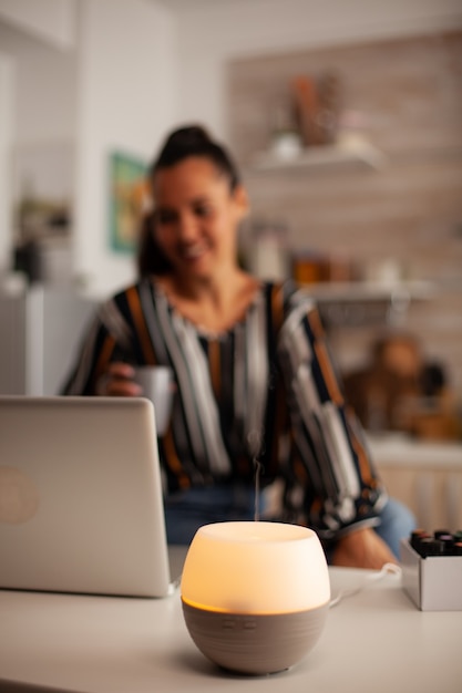 Woman enjoying aromatherapy while working on laptop in kitchen