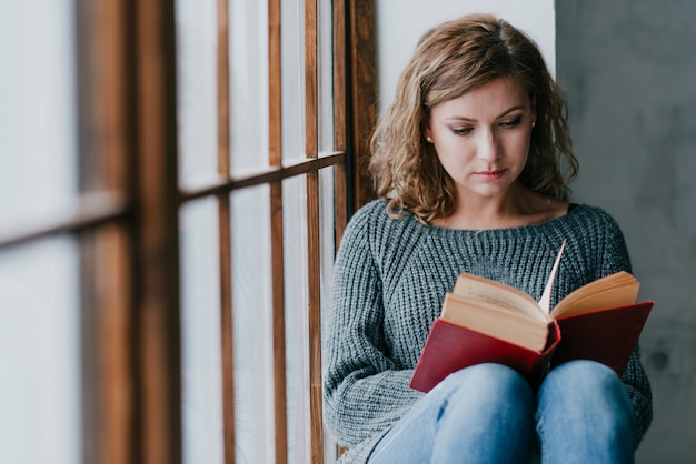 Free photo woman enjoying reading near huge window