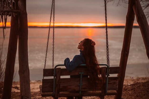 日の出の美しい湖のそばでリラックスした時間を楽しんでいる女性。