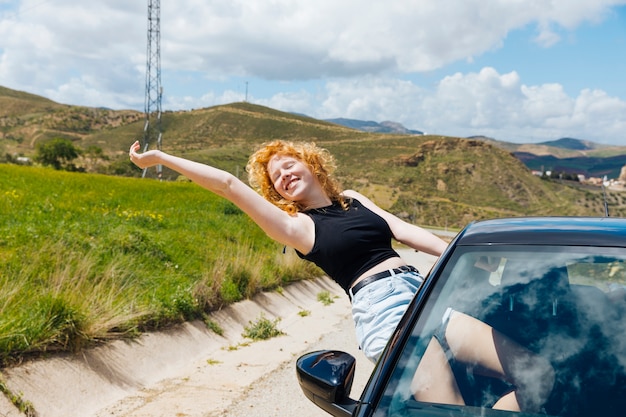 Женщина, наслаждающаяся поездкой из окна автомобиля и протягивающая руку с закрытыми глазами