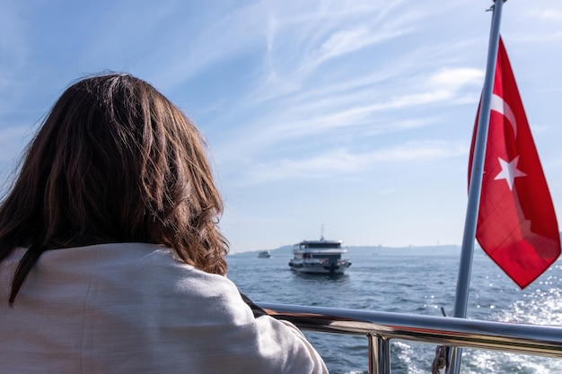 Woman enjoying the view of the boat floating on the Black Sea near the red flag of Turkey