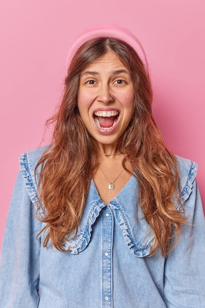 woman exclaims gladfully reacts on something amazing wears headband and denim shirt feels very glad isolated on pink. People and joy