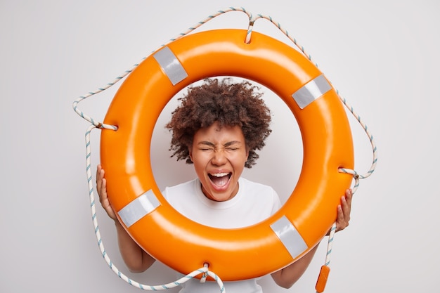 woman exclaims keeps mouth widely opened holds lifebuoy supervises people on water to prevent accident poses with lifeguard equipment on white ready to rescue you