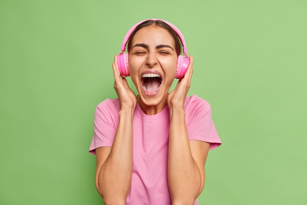 женщина громко восклицает, широко открывает рот слушает музыку с громким звуком в наушниках носит повседневную футболку только на зеленом ознобе