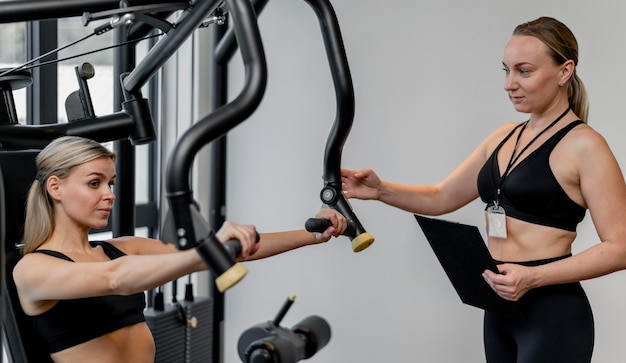 Woman exercising at the gym and coach holding clipboard