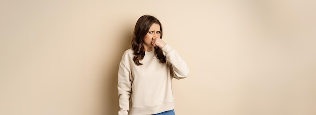 Woman expressing disgust of bad disgusting smell close nose and grimaing from dislike standing over