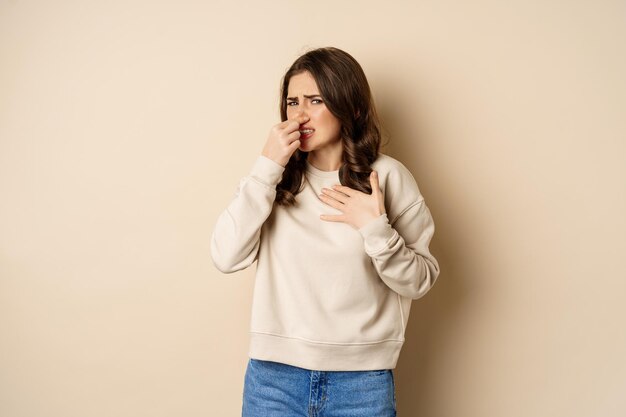 Woman expressing disgust of bad disgusting smell close nose and grimaing from dislike standing over ...