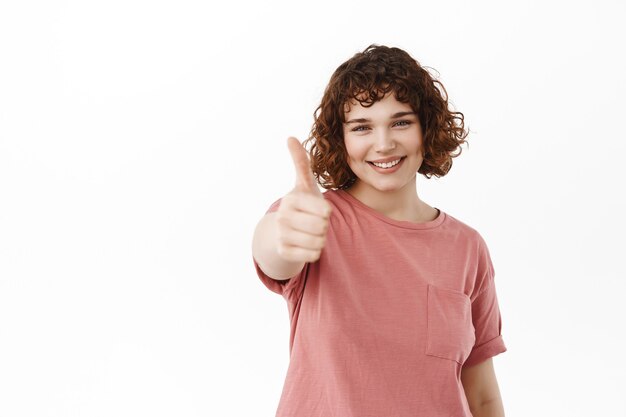 woman extends her hand with thumb up to praise something good, compliment great effort, say yes and approve, standing on white.