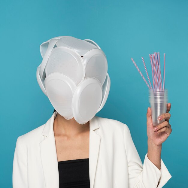 Woman face covered in plastic plates and holding plastic cups and straws