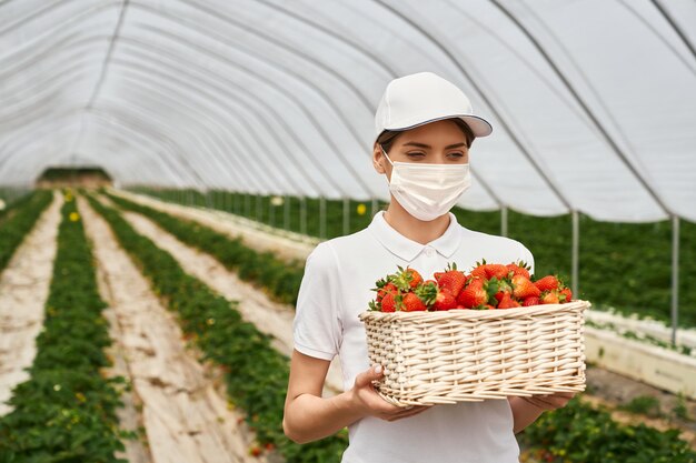 Woman in face mask carrying basket with strawberries