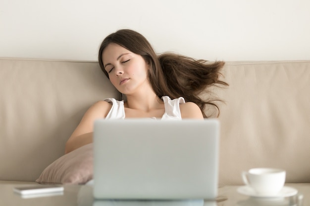 ノートパソコンの前のソファーで眠りに落ちる女性