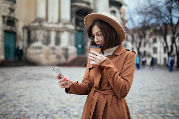 彼女の電話で写真やテキストメッセージで話しているファッション帽子の女性