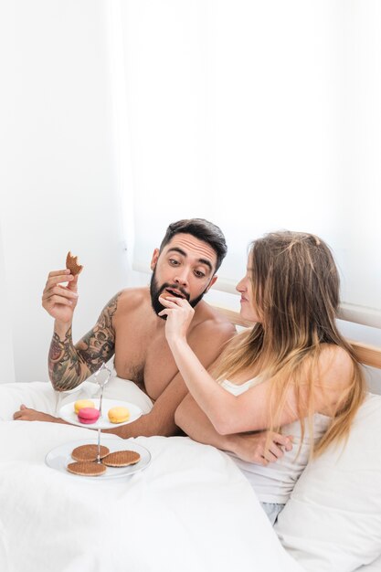 Woman feeding biscuit to man on bed