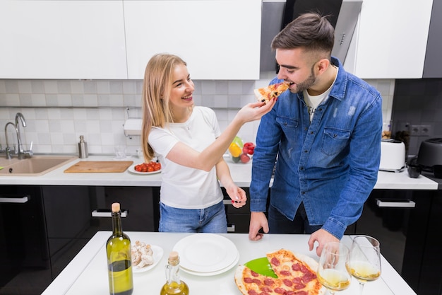 Женщина кормит мужчину с пиццей на кухне