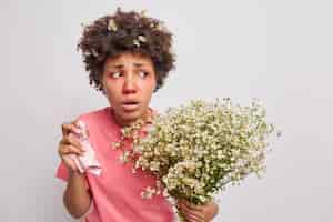 Free photo woman feels unwell suffers from allergy symptoms holds tissue in hand allergic to wildflowers holds bouquet of camomile poses on white