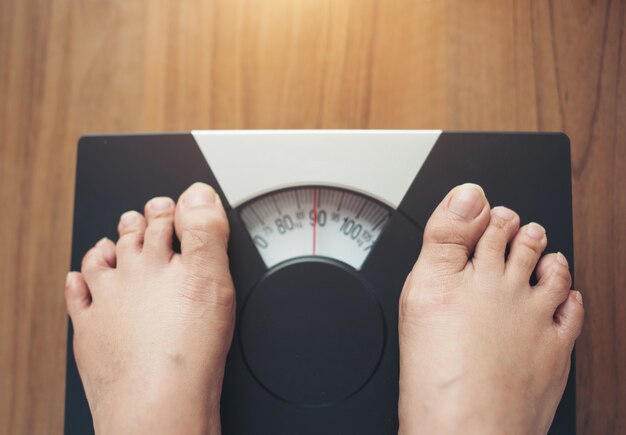 Woman feet standing on Weight Scale on wooden background