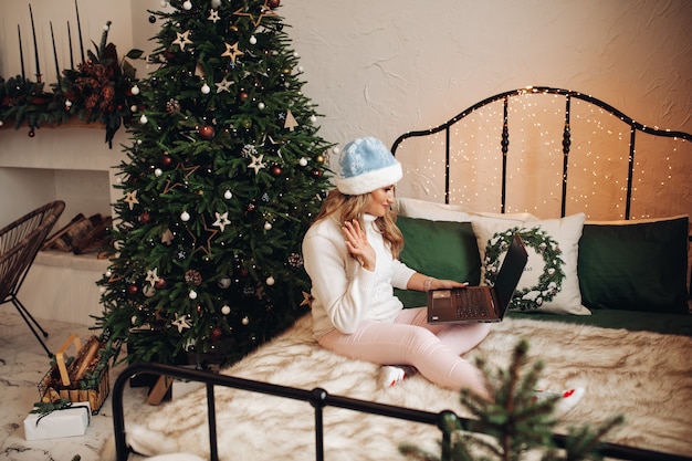 Woman in festive hat waving via laptop.