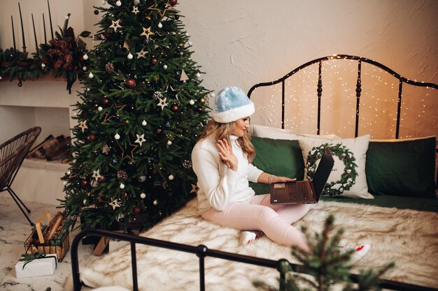 Woman in festive hat waving via laptop.