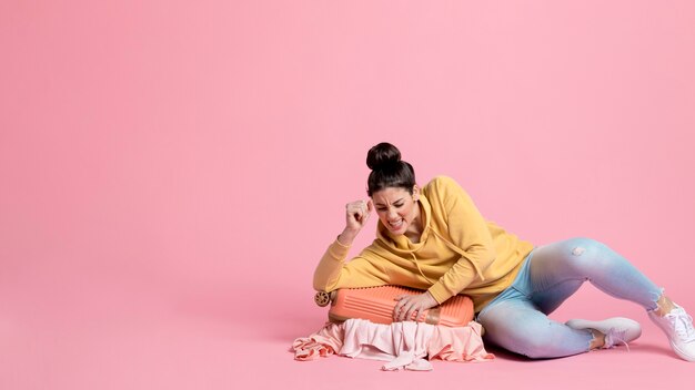 Woman fitting all her clothes in a baggage with copy space