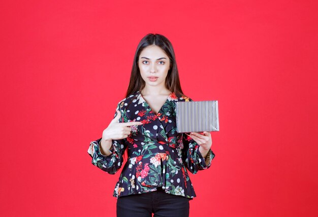 woman in floral shirt holding a silver gift box. 