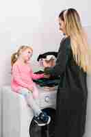 Foto gratuita vestiti pieganti della donna che esaminano sua figlia che si siede sulla lavatrice