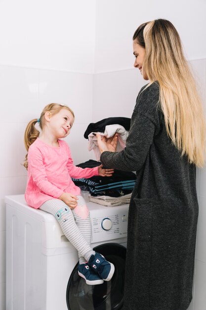 Woman folding clothes looking at her daughter sitting on washing machine