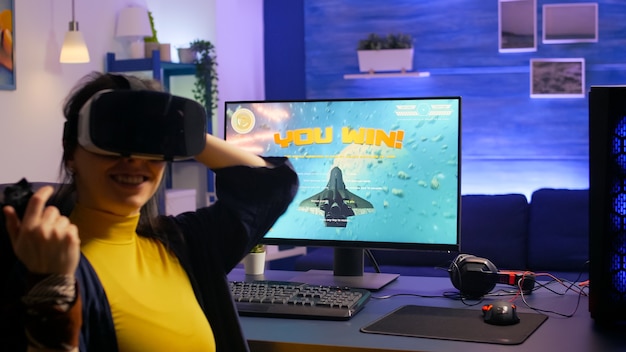 ゲームスタジオでVRヘッドセットを着用しながらスペースシュータービデオゲームに勝つ女性ゲーマー