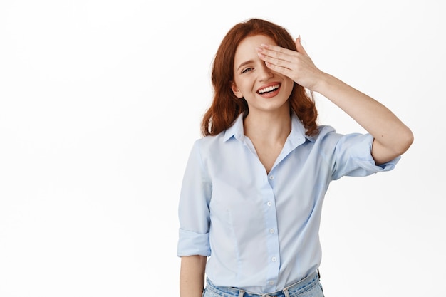 woman gasp from amazement, hide one half of face with palm, staring at something awesome, standing in blouse on white