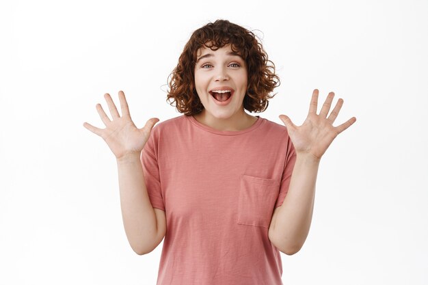 woman, gasping and looking amazed, spread hands sideways and celebrating, staring impressed and surprised at camera, standing on white