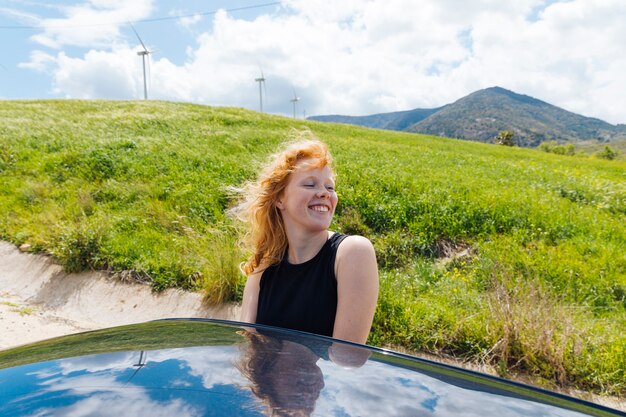Woman getting out of car window and putting face to wind