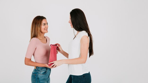 Woman gifting paper bag to girlfriend