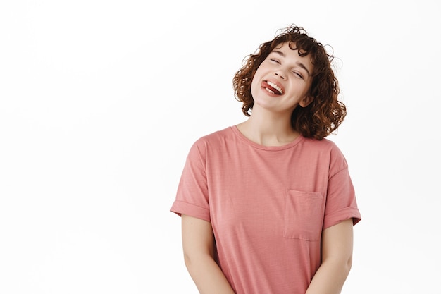 woman, girl shows tongue smiles and laughs, tilts head carefree, enjoy summer holidays, standing positive on white.