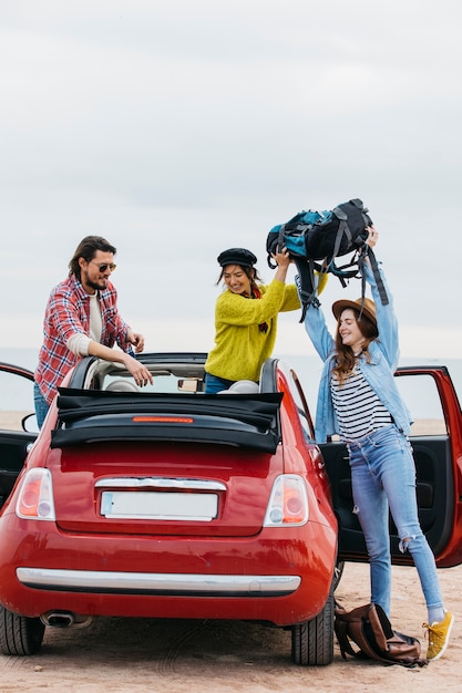 Woman giving backpack to lady near man leaning out from car