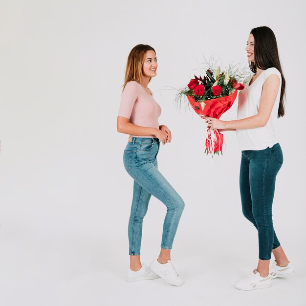 Woman giving bunch of flowers to girlfriend