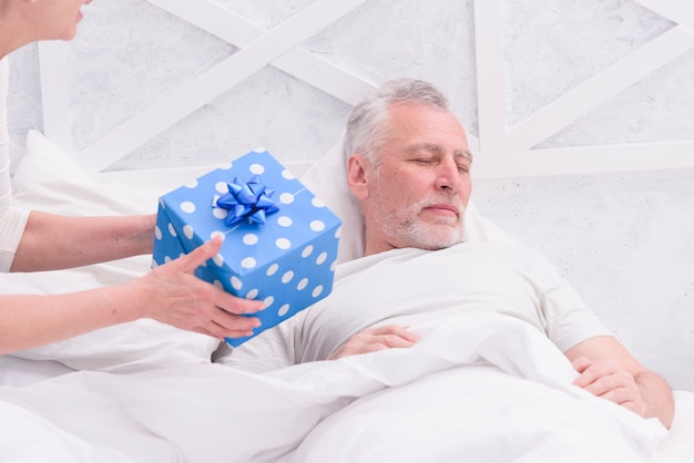 Woman giving gift to her husband sleeping on bed