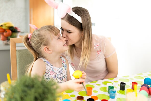 Woman giving kiss to daughter painting eggs