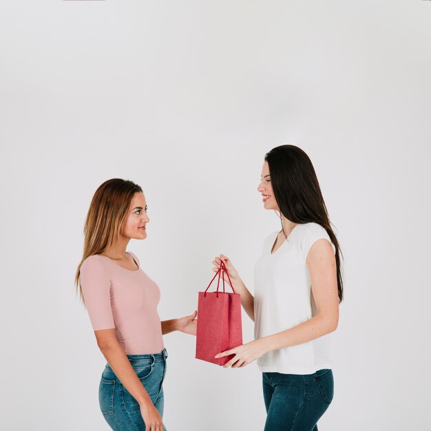 Woman giving paper bag to girlfriend in studio