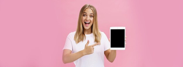 Foto gratuita donna che dà raccomandazione acquista tablet digitale che punta allo schermo del dispositivo con il dito indice sorridente e