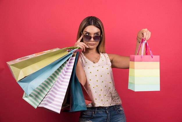 Woman in glasses holding her shopping bags on red wall . 